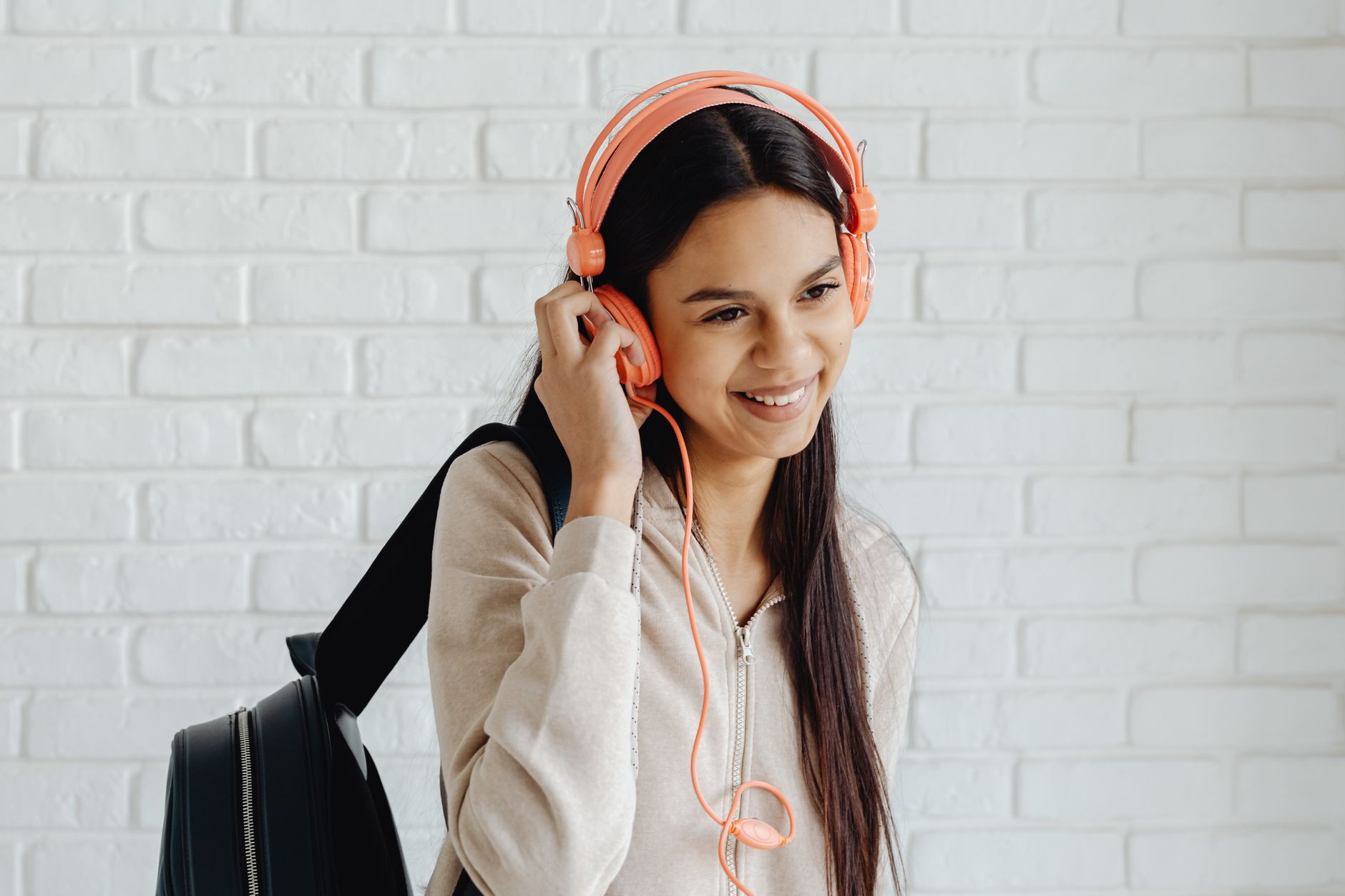Smiling teenager wearing pink headphones, holding backpack indoors.